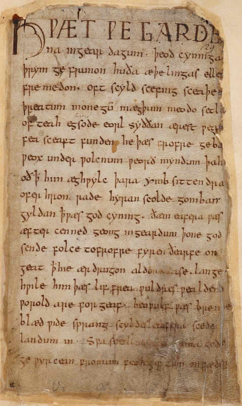 La prima pagina del manoscritto di Beowulf, scritta a mano in inglese antico, con segni di bruciatura lungo i bordi
